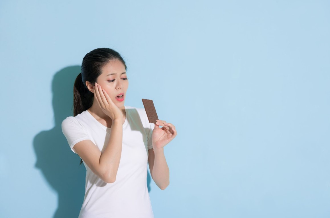 ผู้หญิงจับแก้มด้วยสีหน้าปวดฟันขณะถือช็อกโกแลต